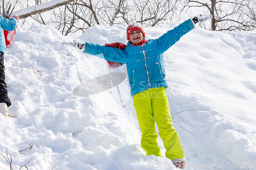 Image of A happy girl stands on the slope of a slide in winter and throws her hands up rejoices at the first snow