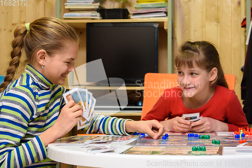 Image of Two girls joyfully laugh while playing board games at the table