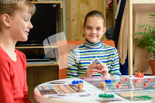 Image of Children in a good mood are playing a board game, one of the girls looked into the frame