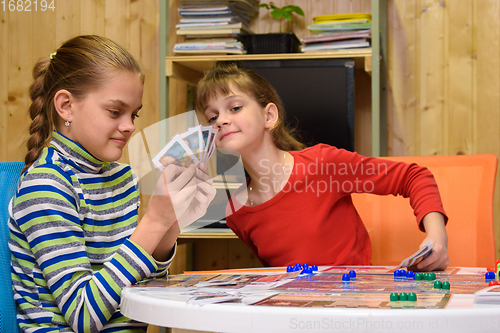 Image of Children play a board game, one of the girls peeps at the cards of the other