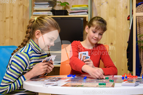 Image of Children play a board game, one of the girls makes the next move, the other watches with a smile