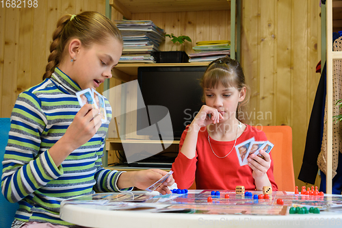 Image of A girl plays a card from her hand, another girl looks thoughtfully