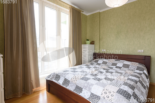 Image of Bedroom interior with a large double bed and a large stained glass window with tulle and curtains