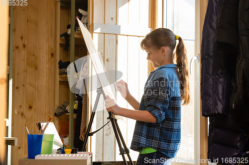 Image of A ten-year-old girl makes a sketch on an easel, removes unnecessary details with a washing eraser