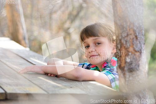 Image of A ten-year-old girl sits at a wooden table in the forest and happily looked into the frame