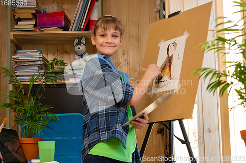 Image of Happy girl at home draws on an easel and happily looked into the frame