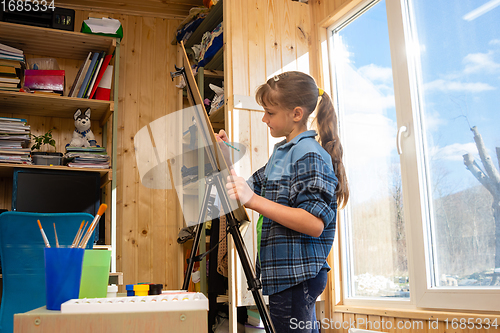 Image of A ten-year-old girl draws on an easel by the wide window of the house