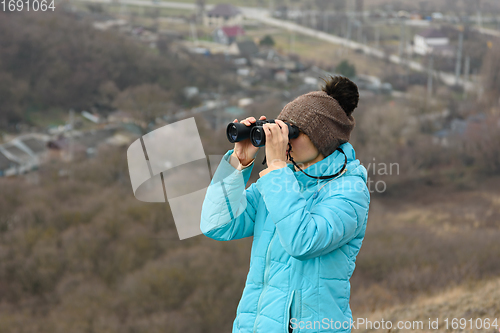 Image of Girl looking through binoculars while standing on top of a mountain on a warm autumn day