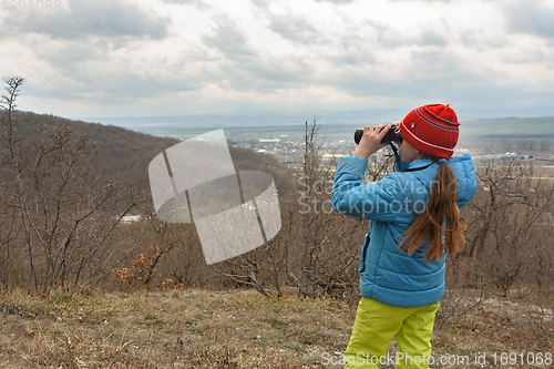 Image of A girl examines a mountain landscape through binoculars, view from the back