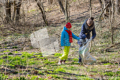 Image of A girl and a woman collect garbage at the forest edge