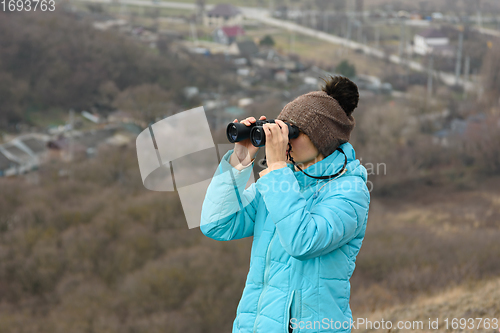 Image of Girl looking through binoculars while standing on top of a mountain on a warm autumn day