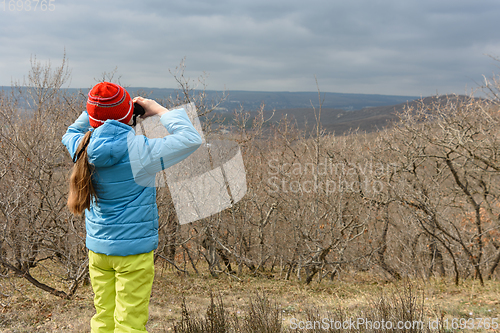 Image of A girl in an autumn day looks through binoculars from the mountain, back view