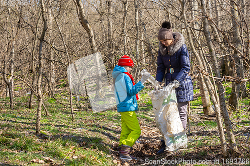 Image of A girl throws a plastic bottle into a trash bag that the girl holds, together they collect garbage in the forest