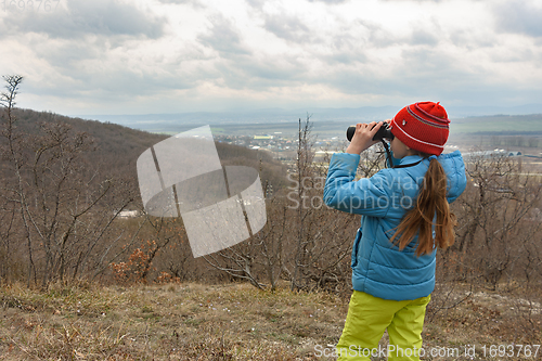 Image of A girl examines a mountain landscape through binoculars, view from the back