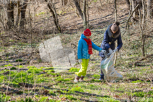 Image of A girl and a woman collect garbage at the forest edge