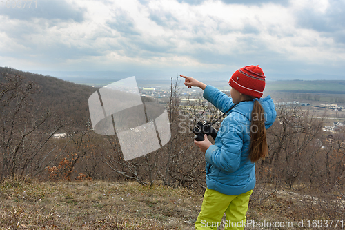 Image of The girl saw something through binoculars, looking at the mountains and points there with her finger