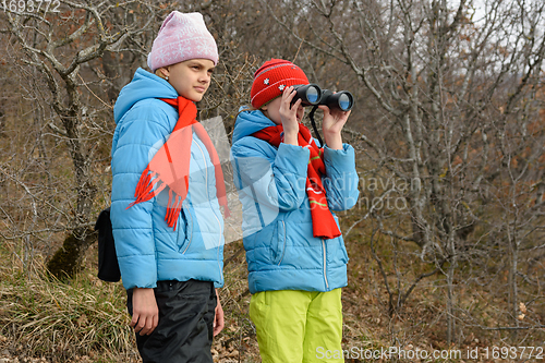 Image of The girl looks with enthusiasm through binoculars, another girl is standing nearby and looks in the same direction