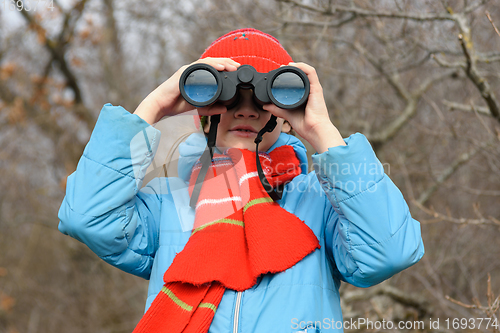 Image of A girl looks through binoculars on a background of a winter forest, front view, close-up