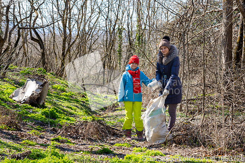 Image of A girl and her daughter collect garbage in the forest in early spring, they looked into the frame