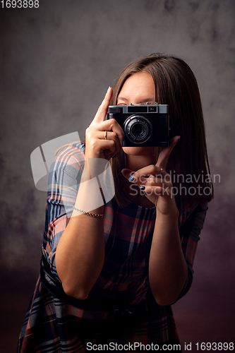 Image of Girl photographer takes pictures with a retro camera, half-length studio portrait on a gray background