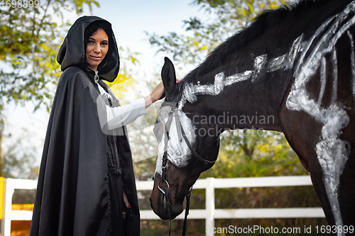 Image of Portrait of a beautiful girl dressed in medieval style, a horse with a painted skeleton is standing next to