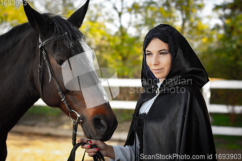 Image of Portrait of a beautiful girl dressed in medieval style, the girl holds a horse by the bridle