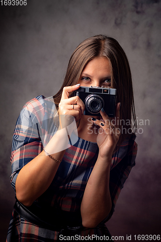 Image of Girl photographer peeking out from behind the camera, half-length studio portrait on a gray background