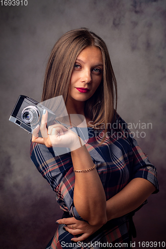 Image of Portrait of a beautiful girl with a camera in her hands, half-length studio portrait on a gray background