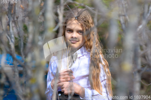 Image of A girl stands with dried wildflowers, in the foreground blurred branches of bushes