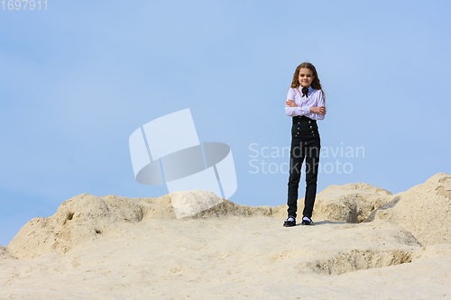 Image of A girl in a white shirt with a bow tie stands on a mountain against the background of the sky