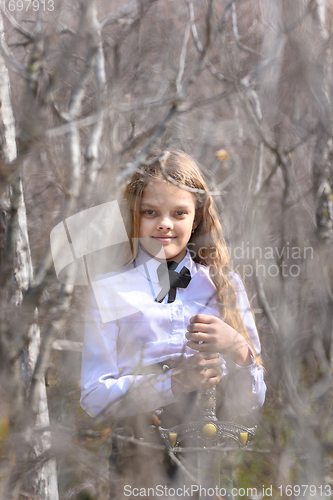 Image of A girl in medieval style clothes stands with a sword, in the foreground and background blurred branches of bushes in the forest