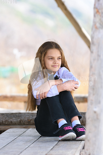 Image of A girl sits on a wooden table and looks into the distance happily and dreamily