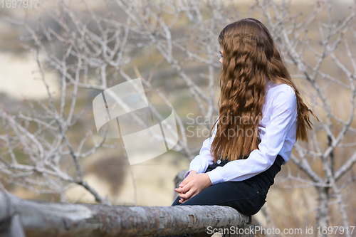 Image of A girl sits on a wooden fence and looks away into the distance