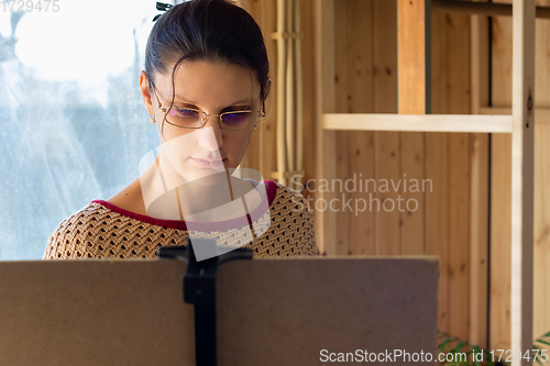 Image of Portrait of an artist at work, a girl draws a drawing on an easel by the window, close-up