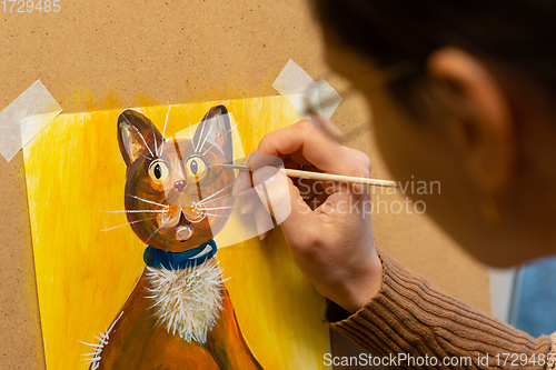 Image of The artist draws with acrylic paints a drawing of a cat on an easel, close-up