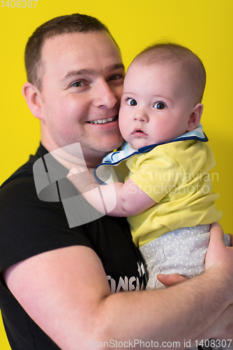 Image of portrait of happy young father holding baby isolated on yellow