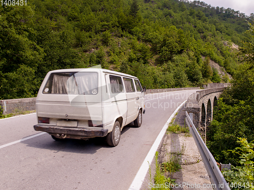 Image of old white van on asphalt road in beautiful countryside