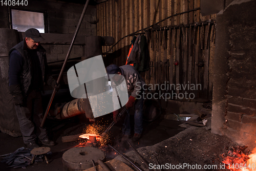 Image of blacksmith workers using mechanical hammer at workshop