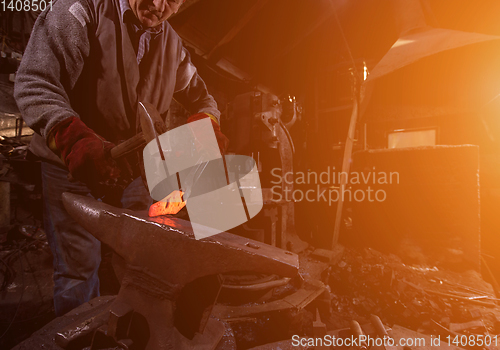 Image of blacksmith manually forging the molten metal with sunlight throu