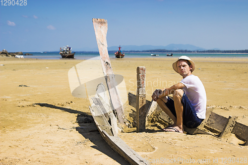 Image of Young stranger sitting on the shattered boat and looking around