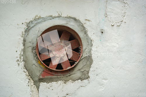 Image of Old rusty fan inserted into wall
