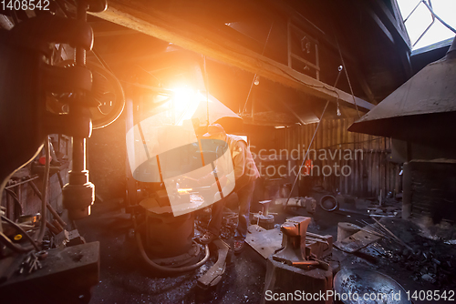 Image of blacksmith manually forging the molten metal with sunlight throu