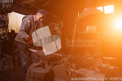 Image of blacksmith manually forging the molten metal with sunlight throu