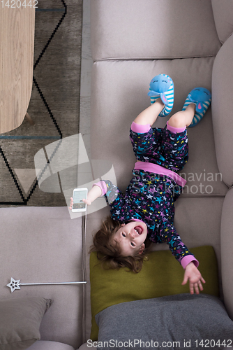 Image of top view of little girl using a smartphone on the sofa