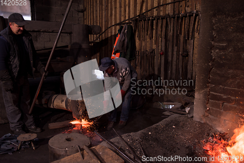 Image of blacksmith workers using mechanical hammer at workshop