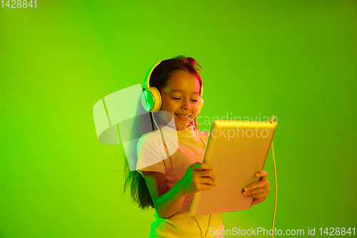 Image of Portrait of little girl in headphones on green background in neon light