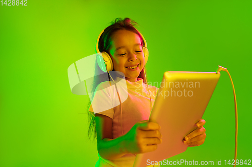 Image of Portrait of little girl in headphones on green background in neon light