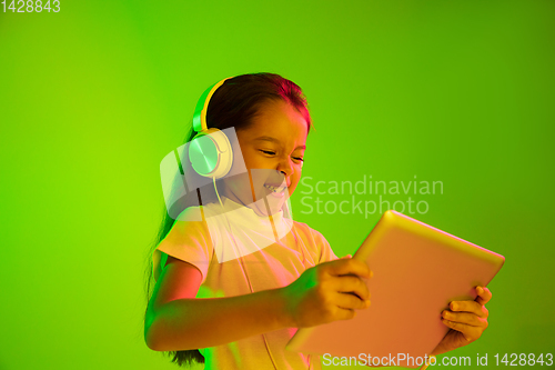 Image of Portrait of little girl in headphones on green background in neon light