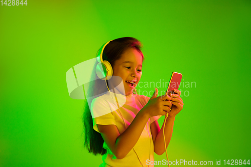 Image of Portrait of little girl in headphones on green background in neon light