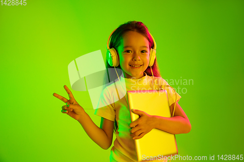 Image of Portrait of little girl in headphones on green background in neon light